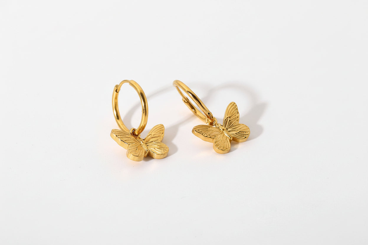 Gold butterfly earrings on a light stone background