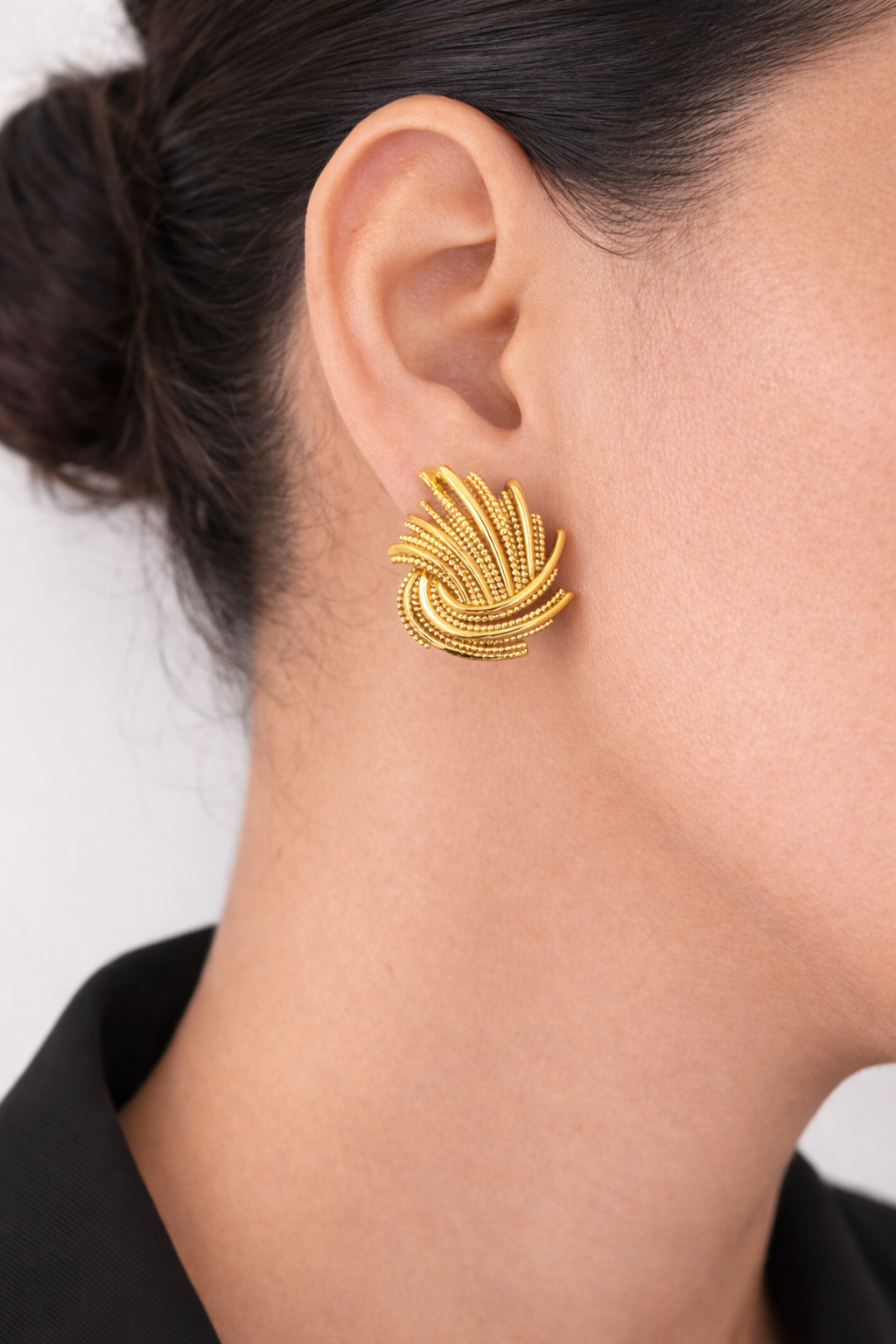 Gold earring worn by a person with a neutral background