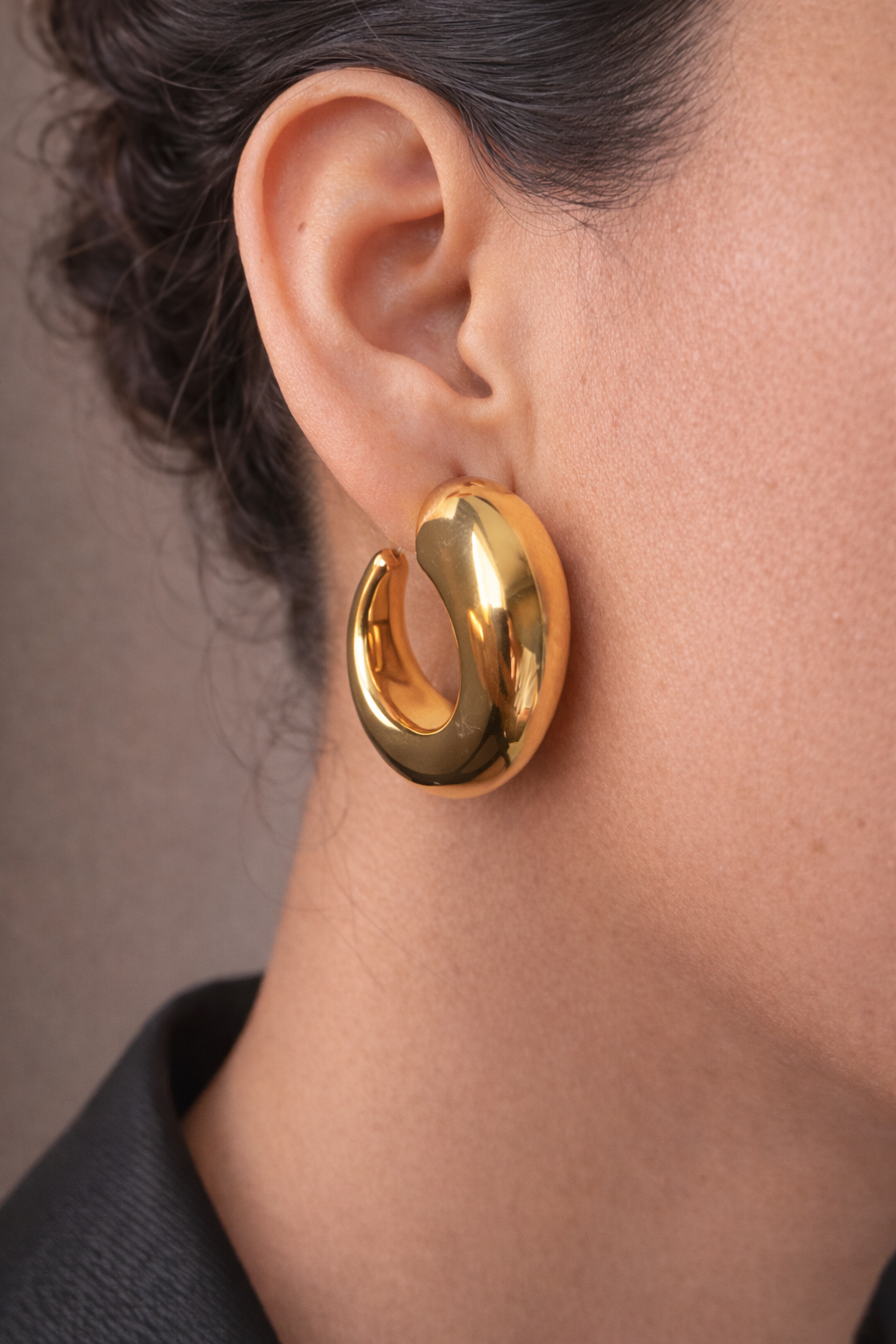 Gold hoop earring worn by a person with a neutral background