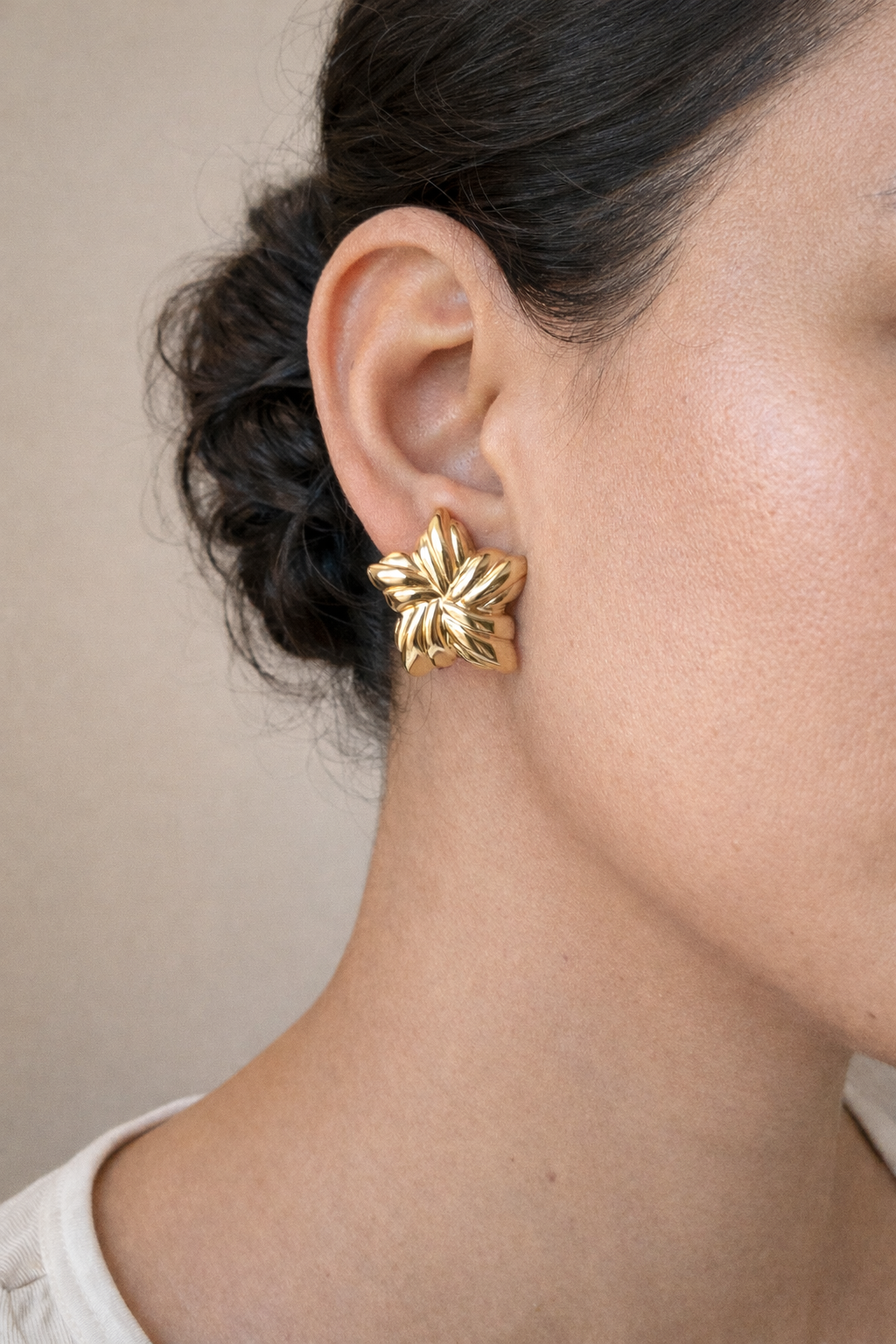 Gold leaf-shaped earring worn by a person against a neutral background