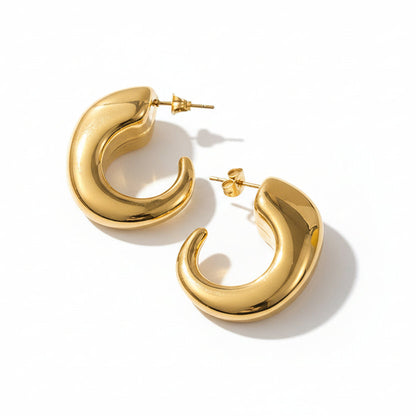 A pair of gold-colored chunky C-hoop earrings on a textured background.