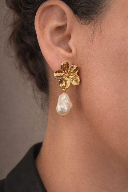 Gold flower earring with pearl drop worn by a person