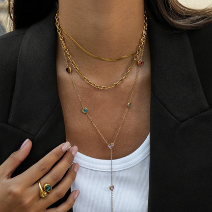 Close-up of a person wearing multiple gold necklaces with gemstones, holding a hand with a ring.